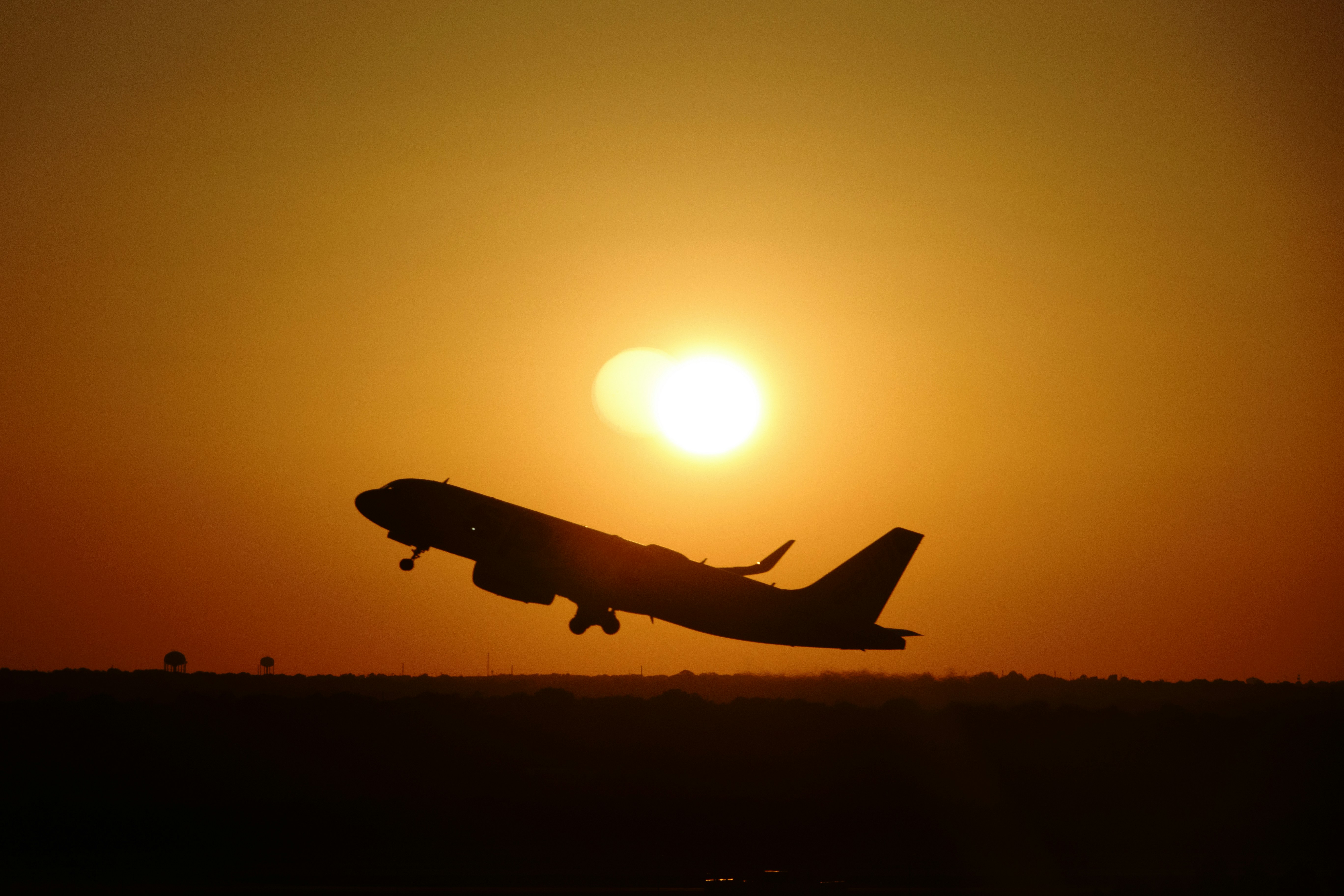 a plane flying in the air at sunset, Airliner takes off silhouetted against the sun.