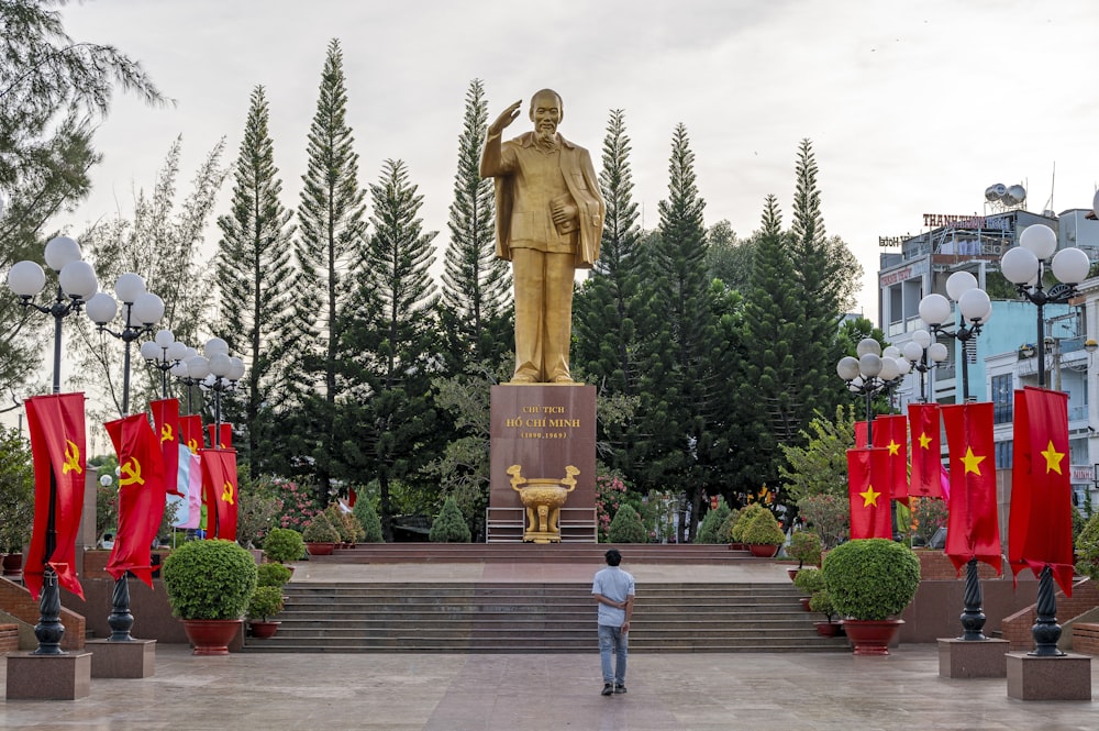 Un hombre de pie frente a una estatua de un hombre sosteniendo una bandera