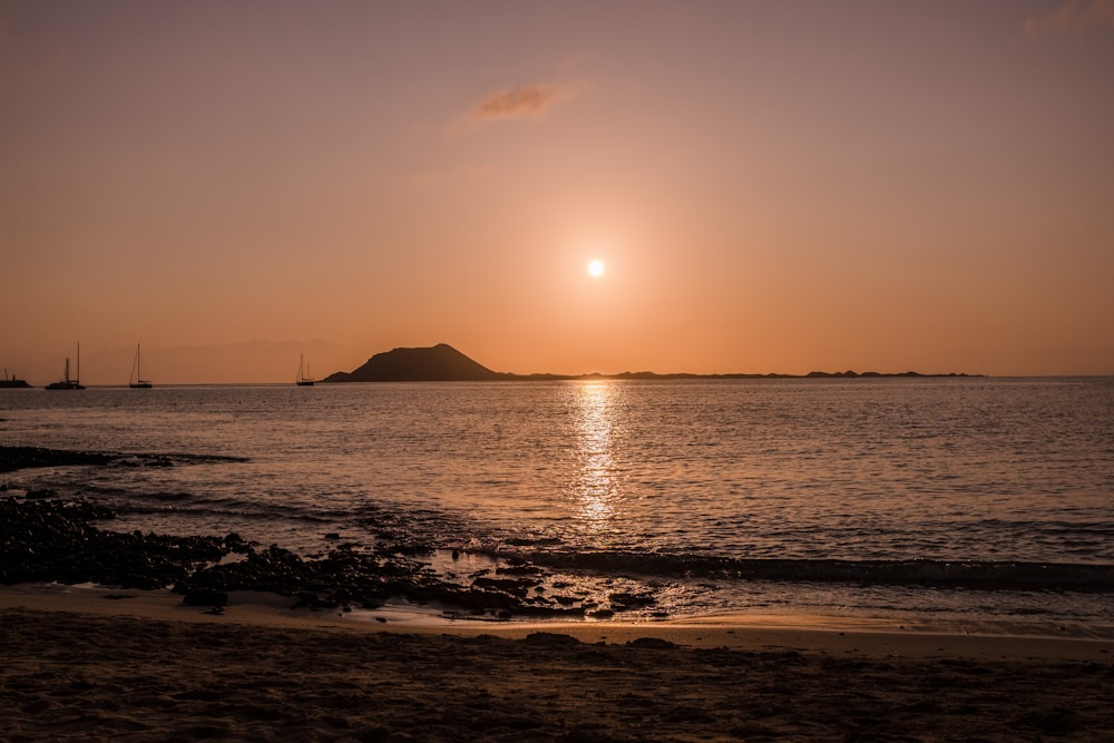 the sun is setting over the water at the beach