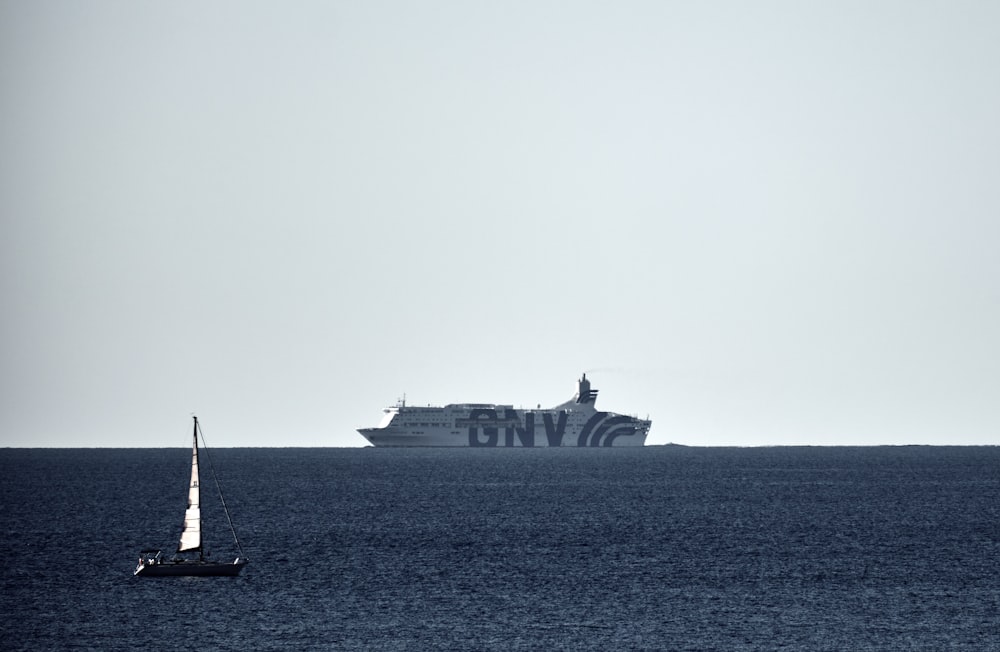 a sailboat in the ocean with a large ship in the background