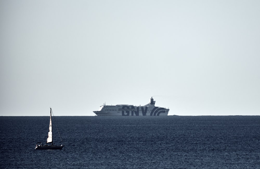 una barca a vela nell'oceano con una grande nave sullo sfondo