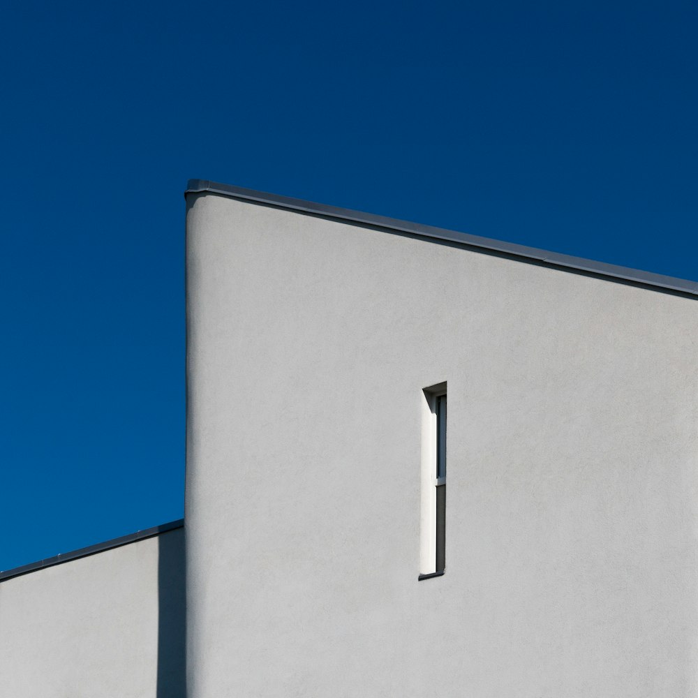 a white building with a window and a blue sky in the background