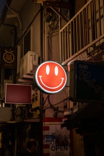 a red smiley face sign hanging from the side of a building