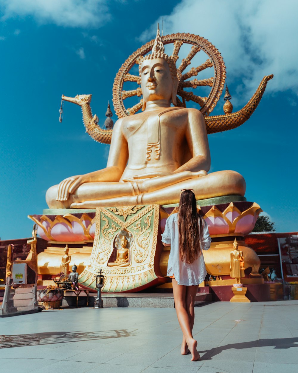 a woman standing in front of a golden buddha statue