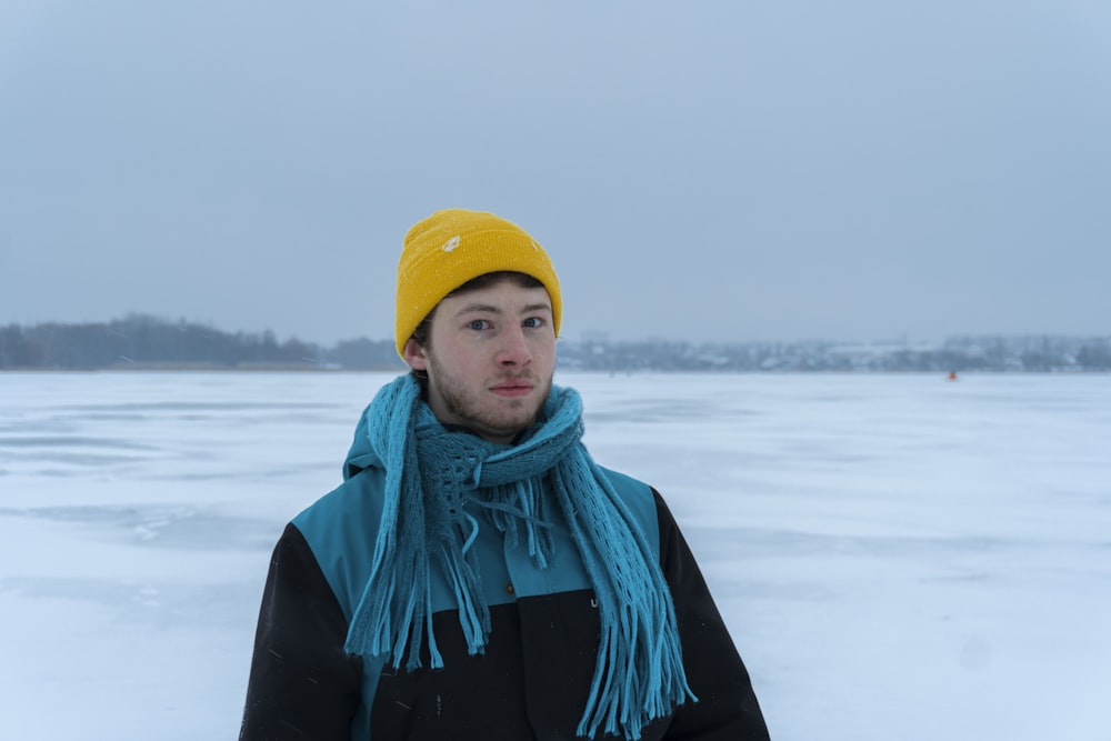 a man wearing a yellow hat and scarf standing in the snow