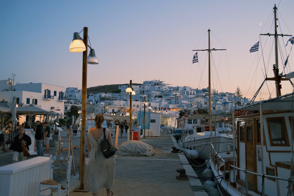 a group of people walking along a pier next to boats