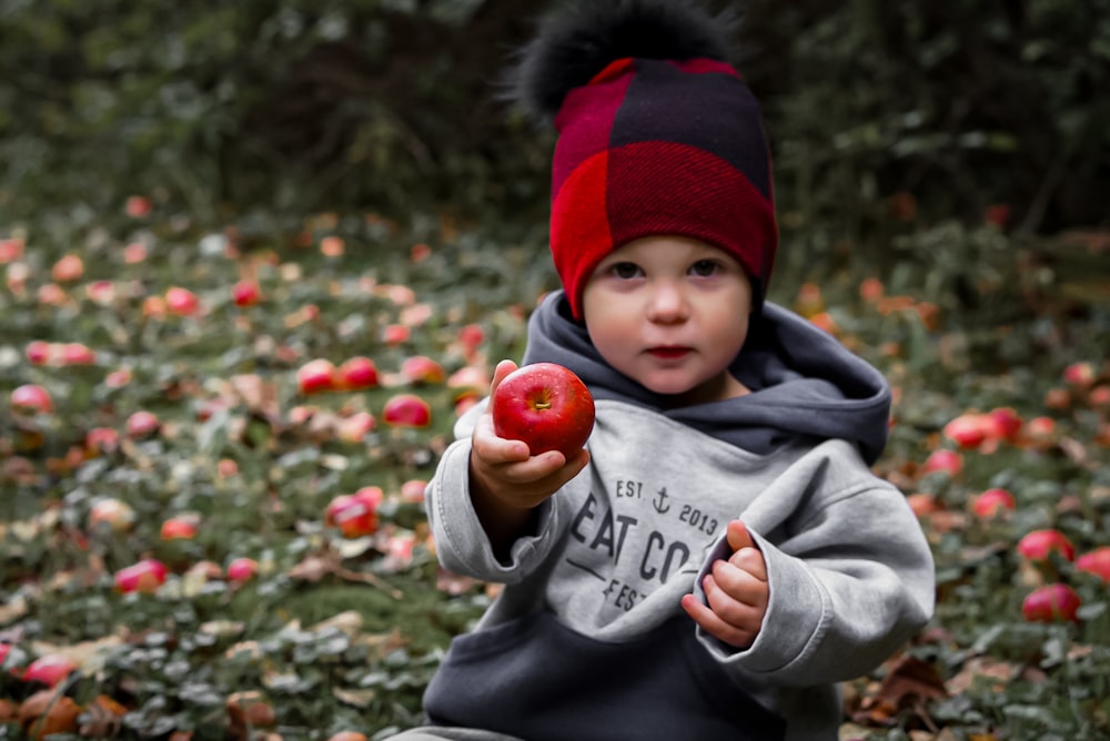 a little boy sitting on the ground holding an apple