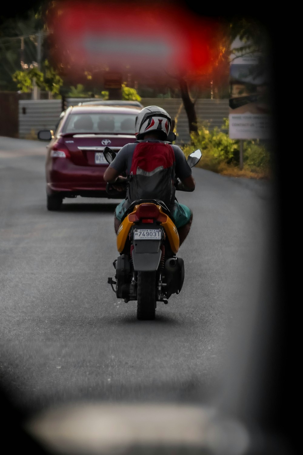Un hombre conduciendo una motocicleta por una calle junto a un coche rojo