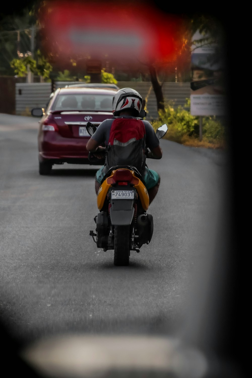 a man riding a motorcycle down a street next to a red car