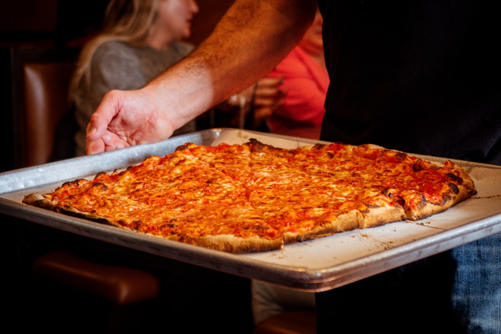 a person holding a tray with a pizza on it