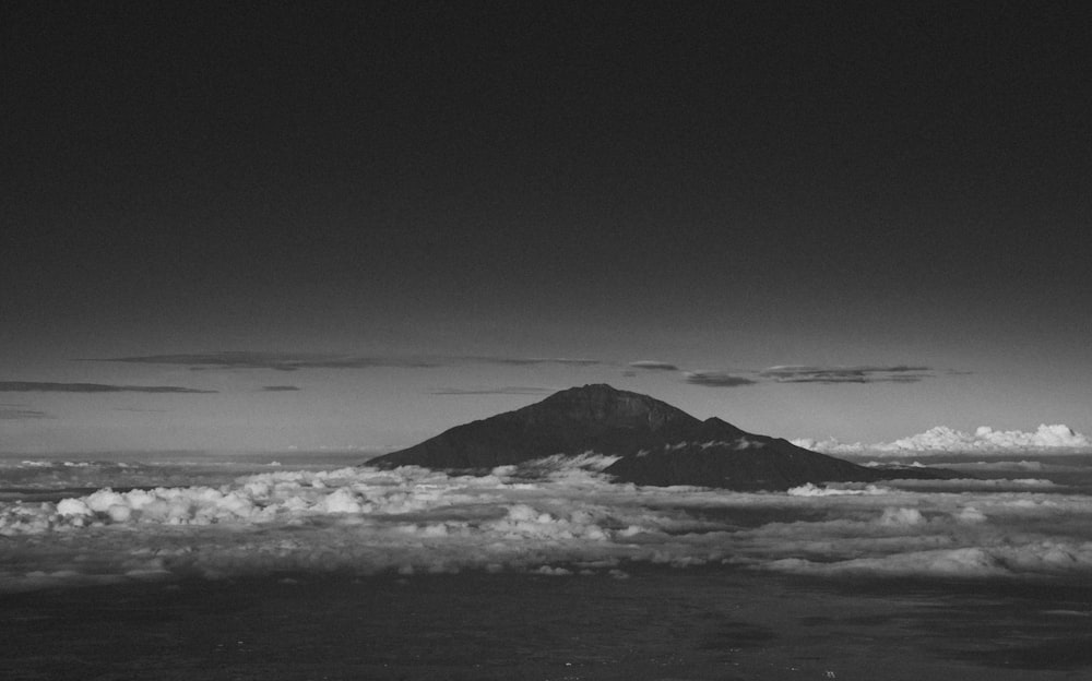 a black and white photo of a mountain and clouds