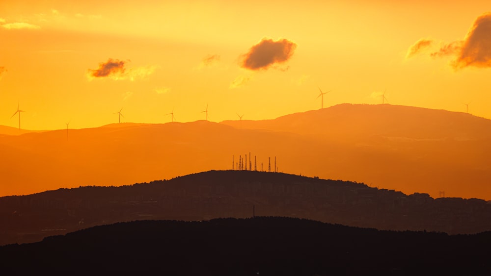 the sun is setting over the hills and windmills