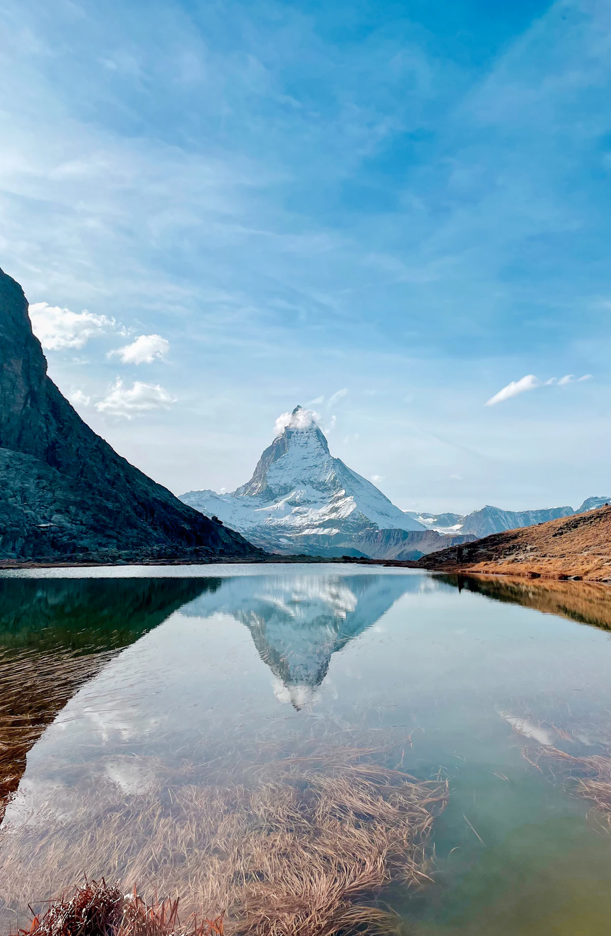 The Matterhorn reflected in a still mountain lake, with dry grass along the shore