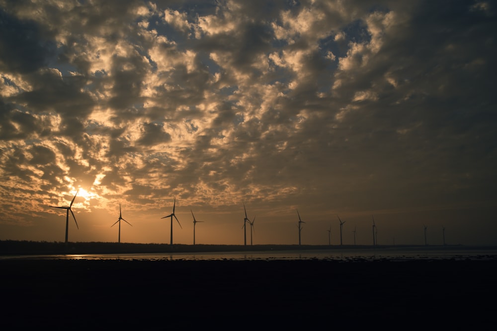 eine Gruppe von Windmühlen in der Ferne mit einem Sonnenuntergang im Hintergrund