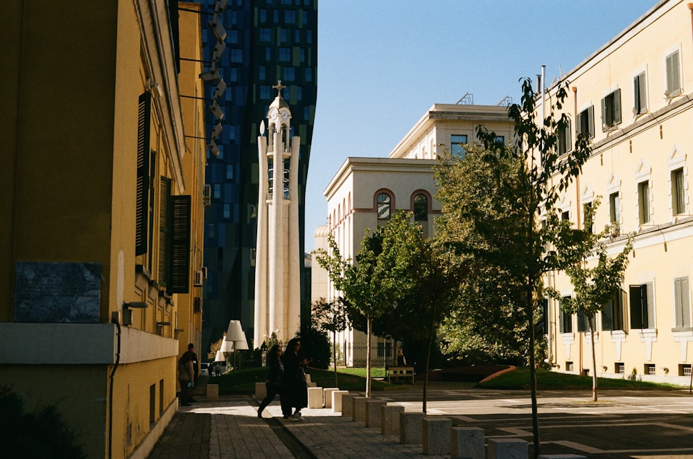 a couple of people walking down a street next to tall buildings