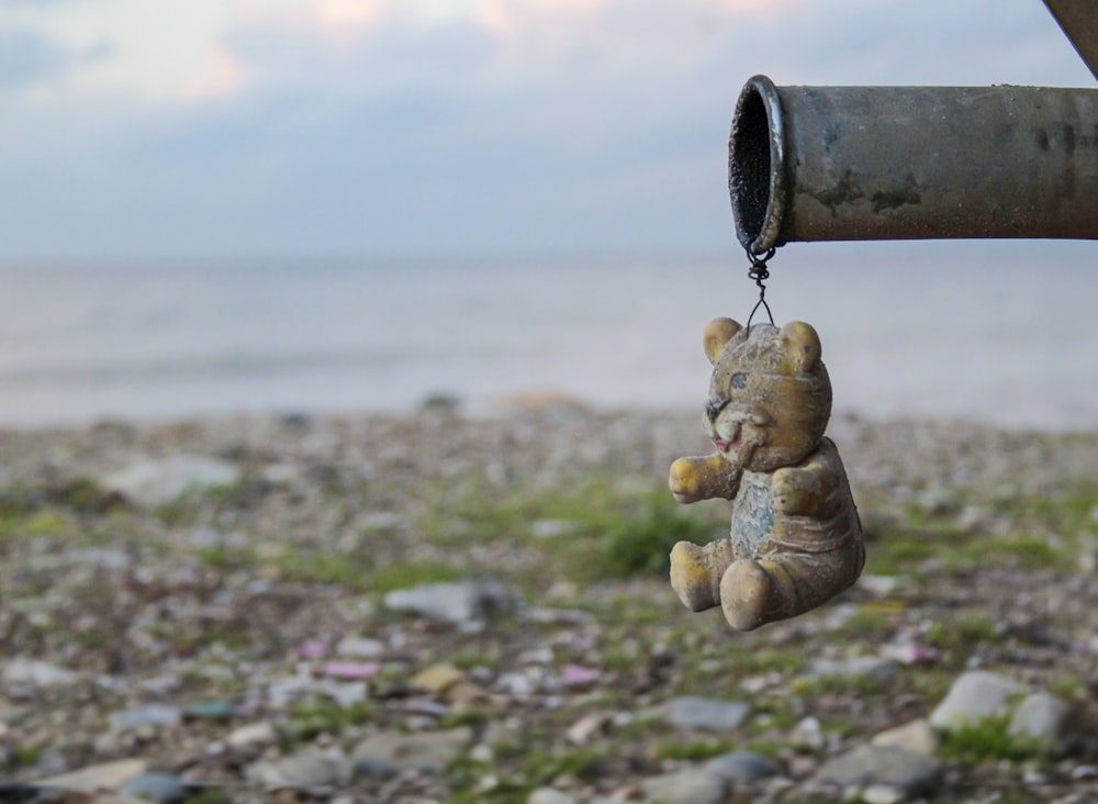 a teddy bear hanging from a pipe near a body of water