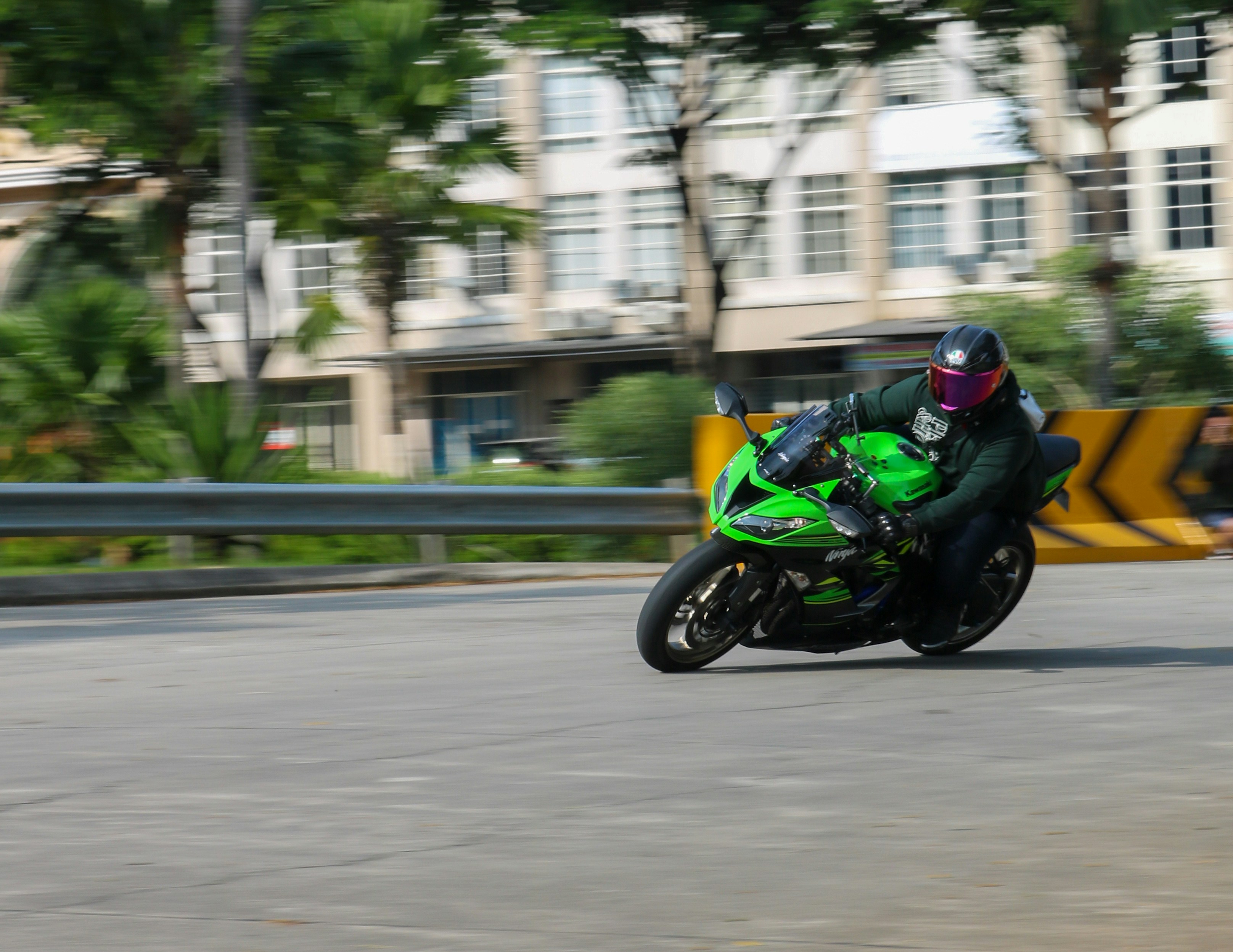Pengendara berhelm menikung dengan motor sport hijau di jalan beraspal