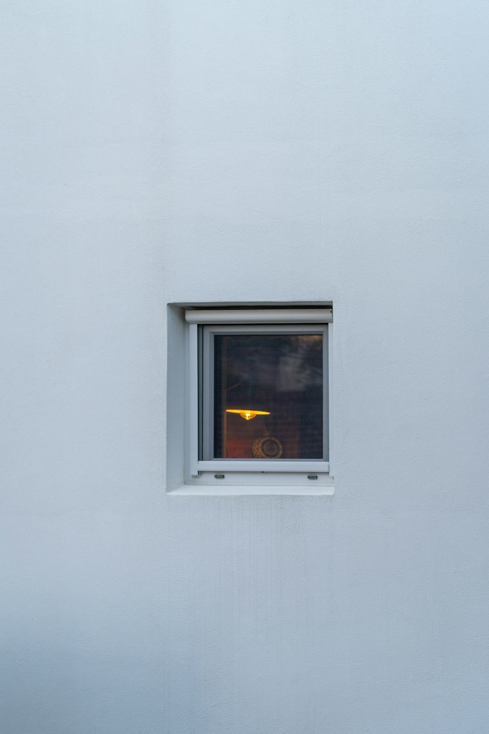 a white wall with a window and a cat sitting on the window sill