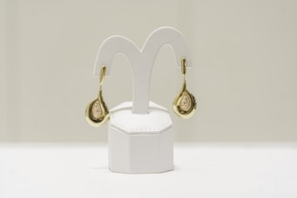 a pair of gold and diamond earrings on a white stand