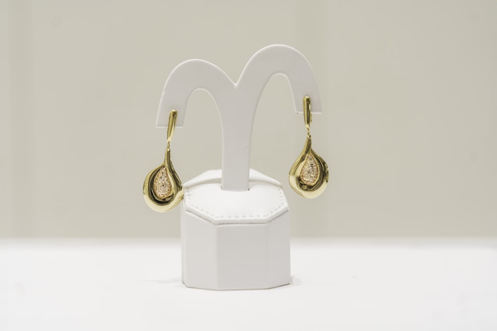 a pair of gold and diamond earrings on a white stand