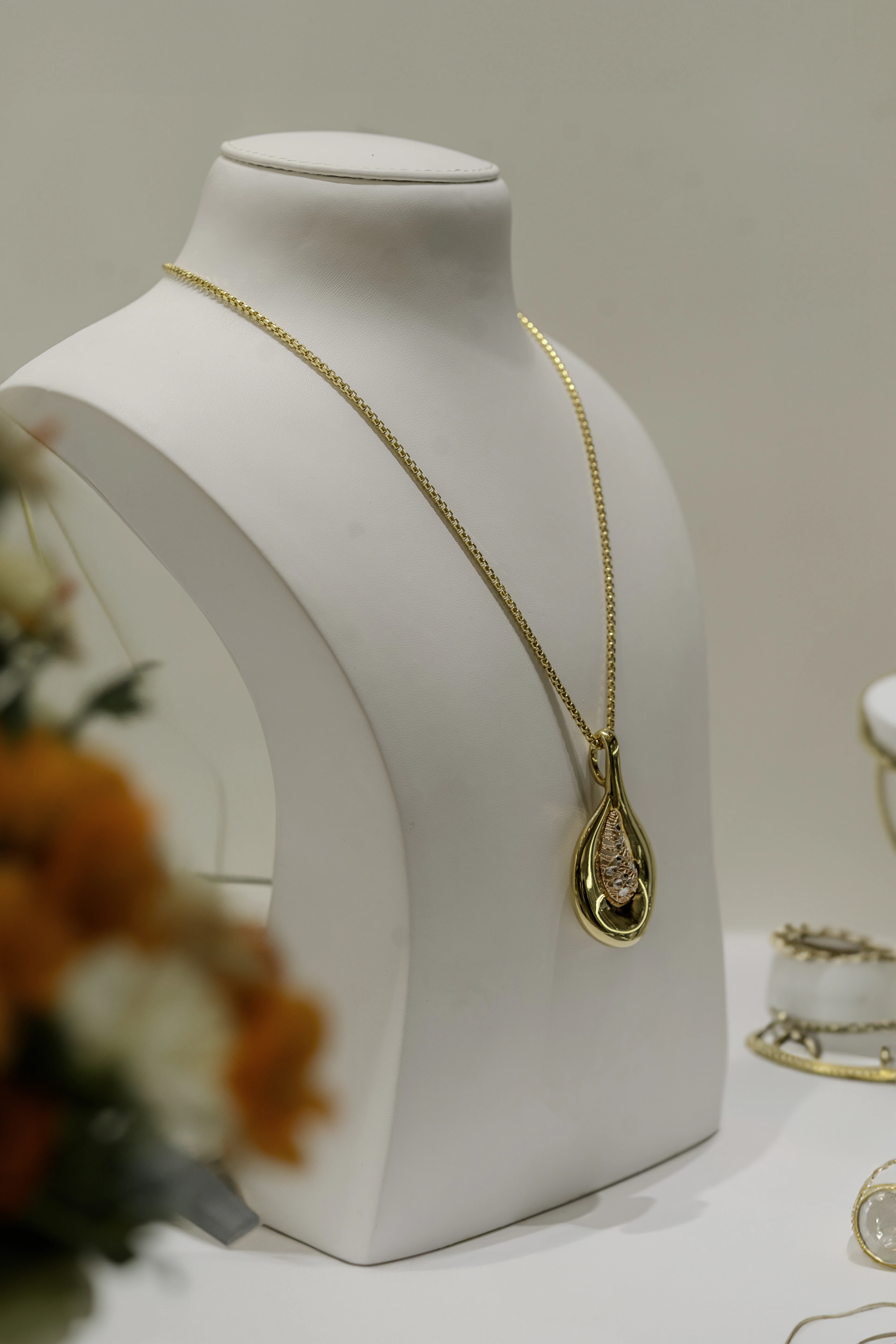 Gold pendant necklace on a display bust beside orange flowers