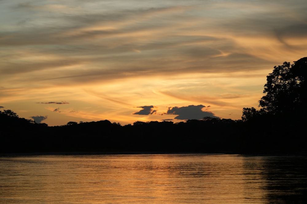 the sun is setting over a lake with trees in the background