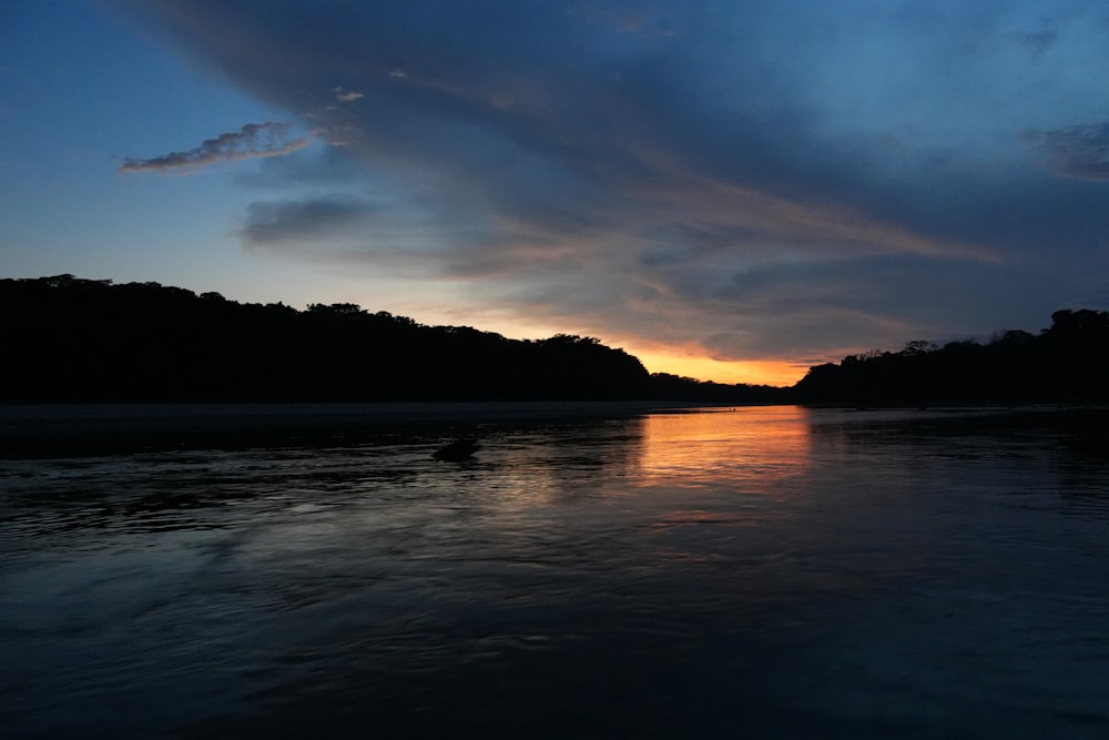 the sun is setting over a river with a boat in the water