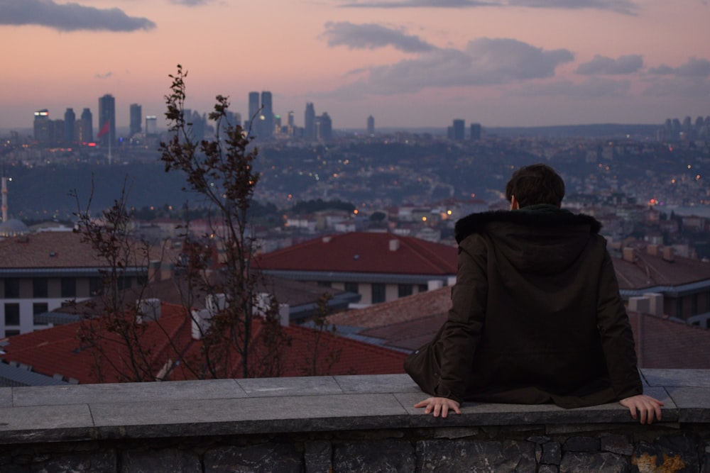 a person sitting on a ledge overlooking a city