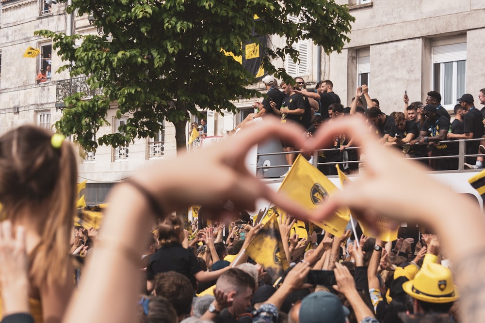 a crowd of people holding up their hands in the shape of a heart