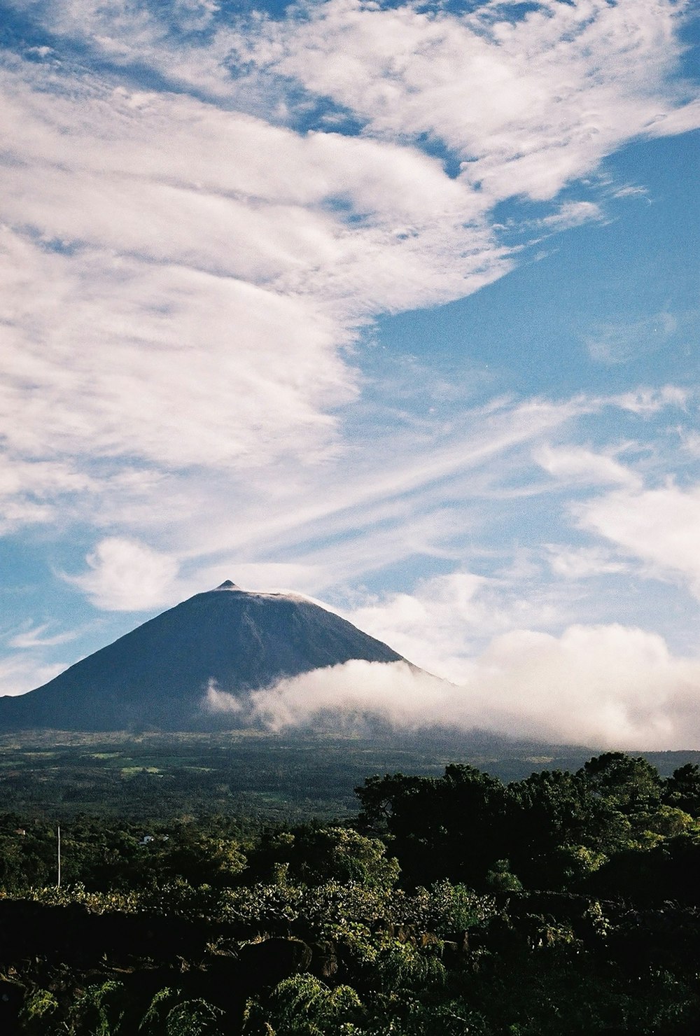 a very tall mountain surrounded by trees and clouds