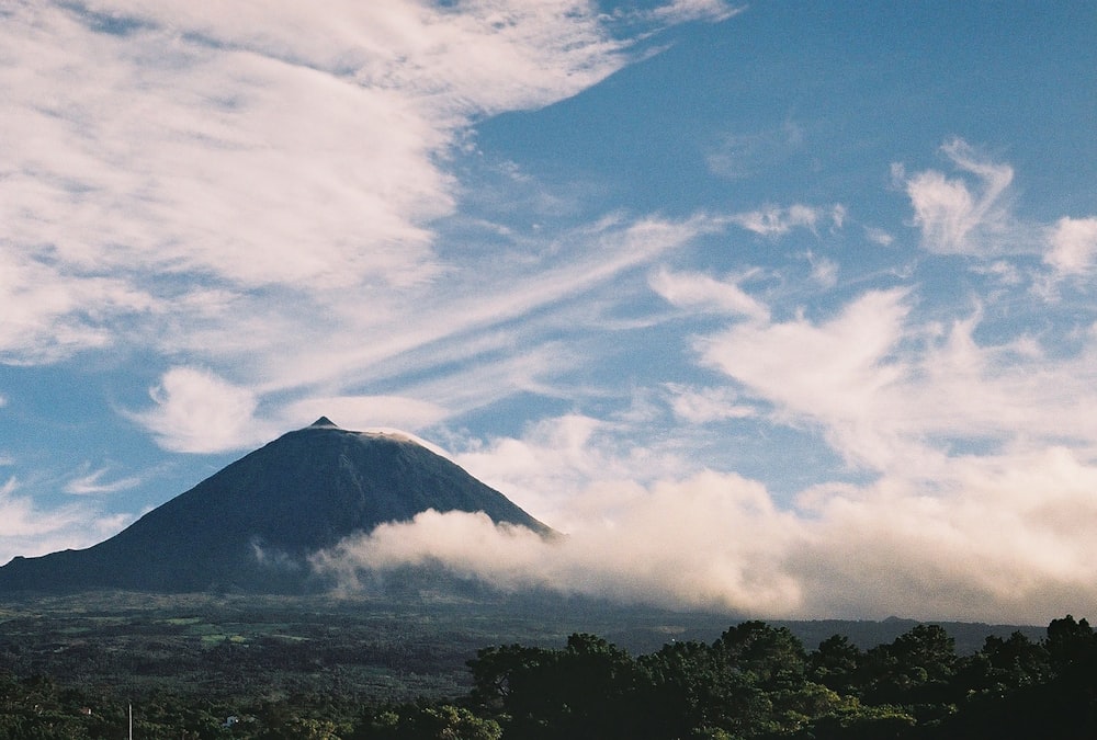 a very tall mountain surrounded by clouds and trees