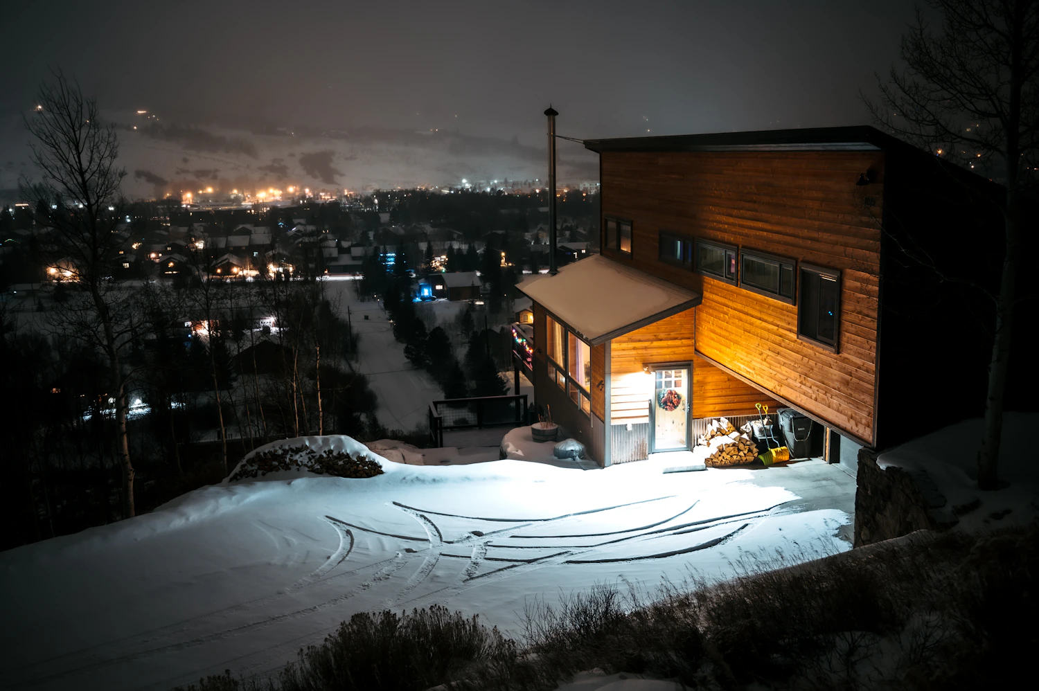 Timber house glowing warm at night above a snowy valley