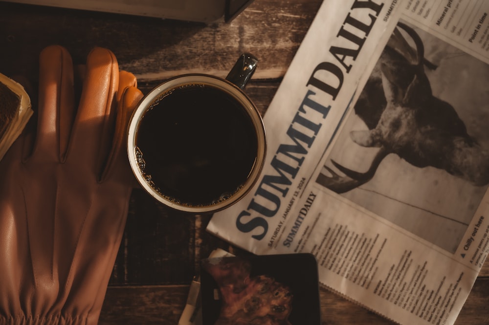 a cup of coffee next to a newspaper and a pair of gloves