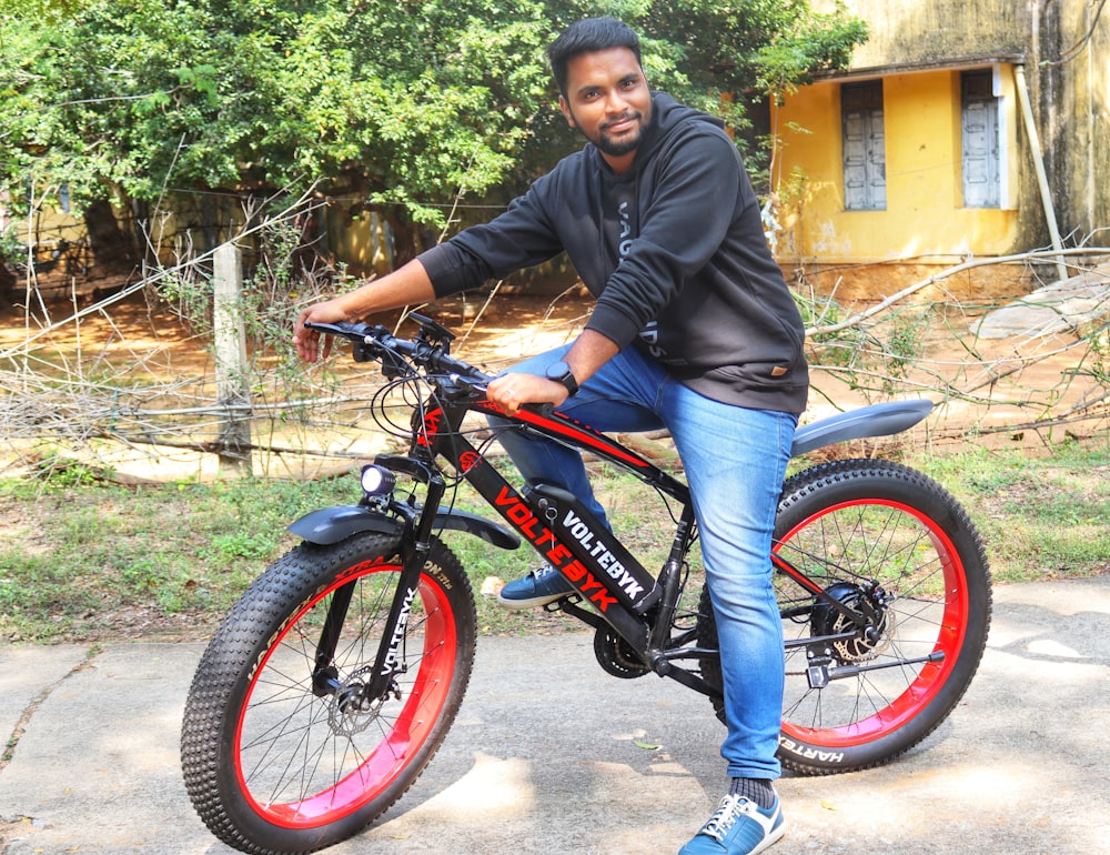 a man sitting on top of a black and red bike