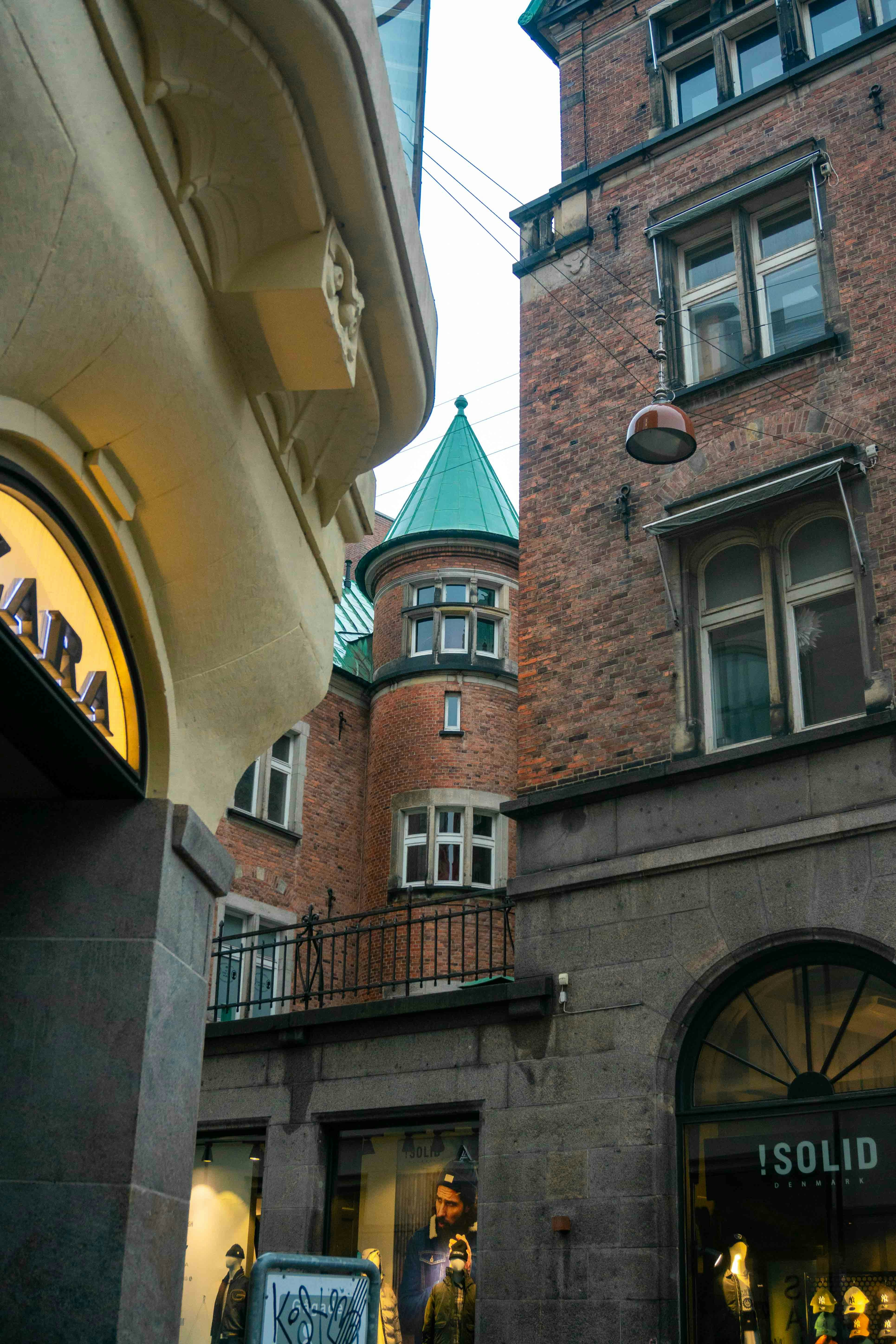 A brick building with a green turret between two stone storefronts