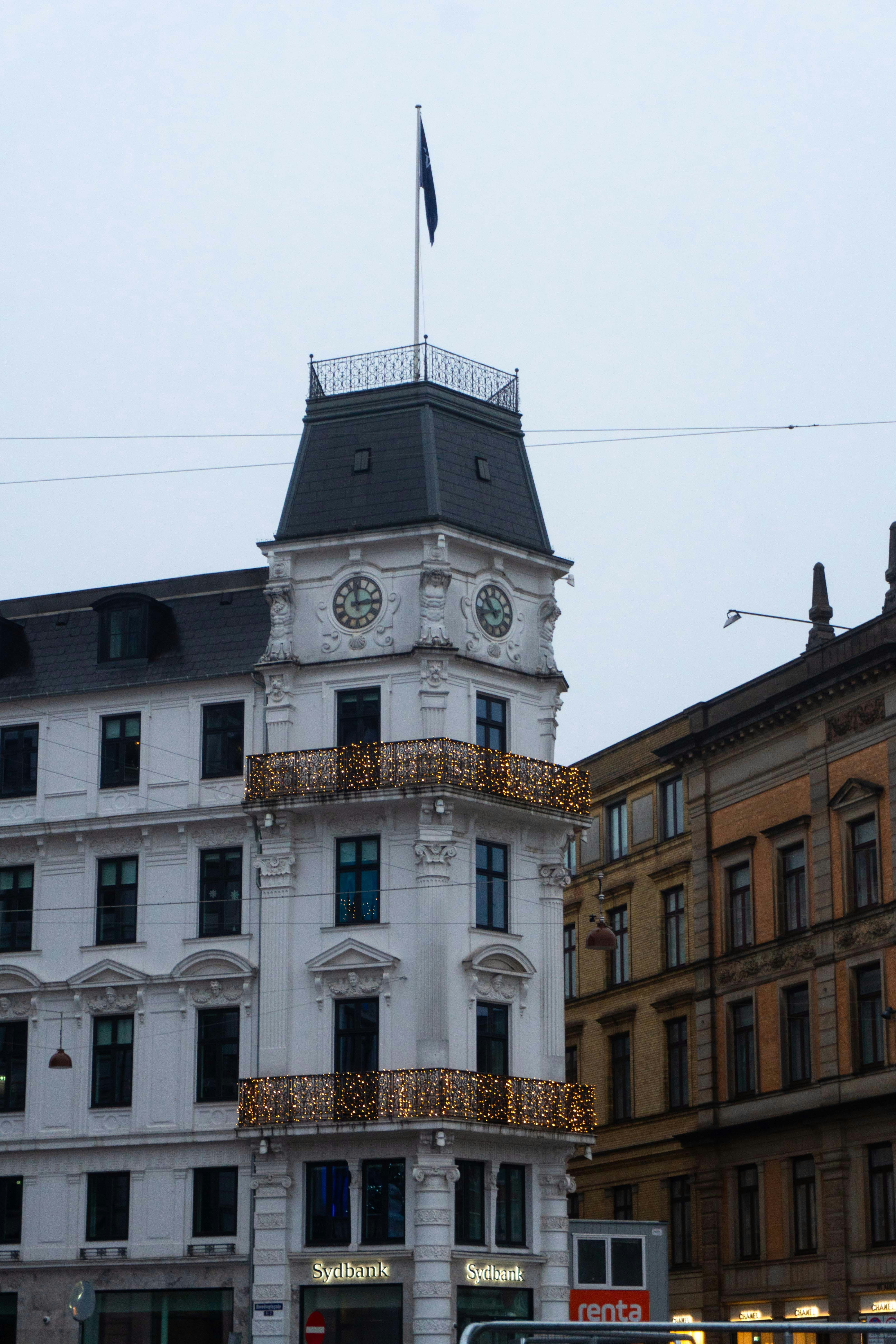 A white corner building with a clock tower and illuminated balconies in Copenhagen