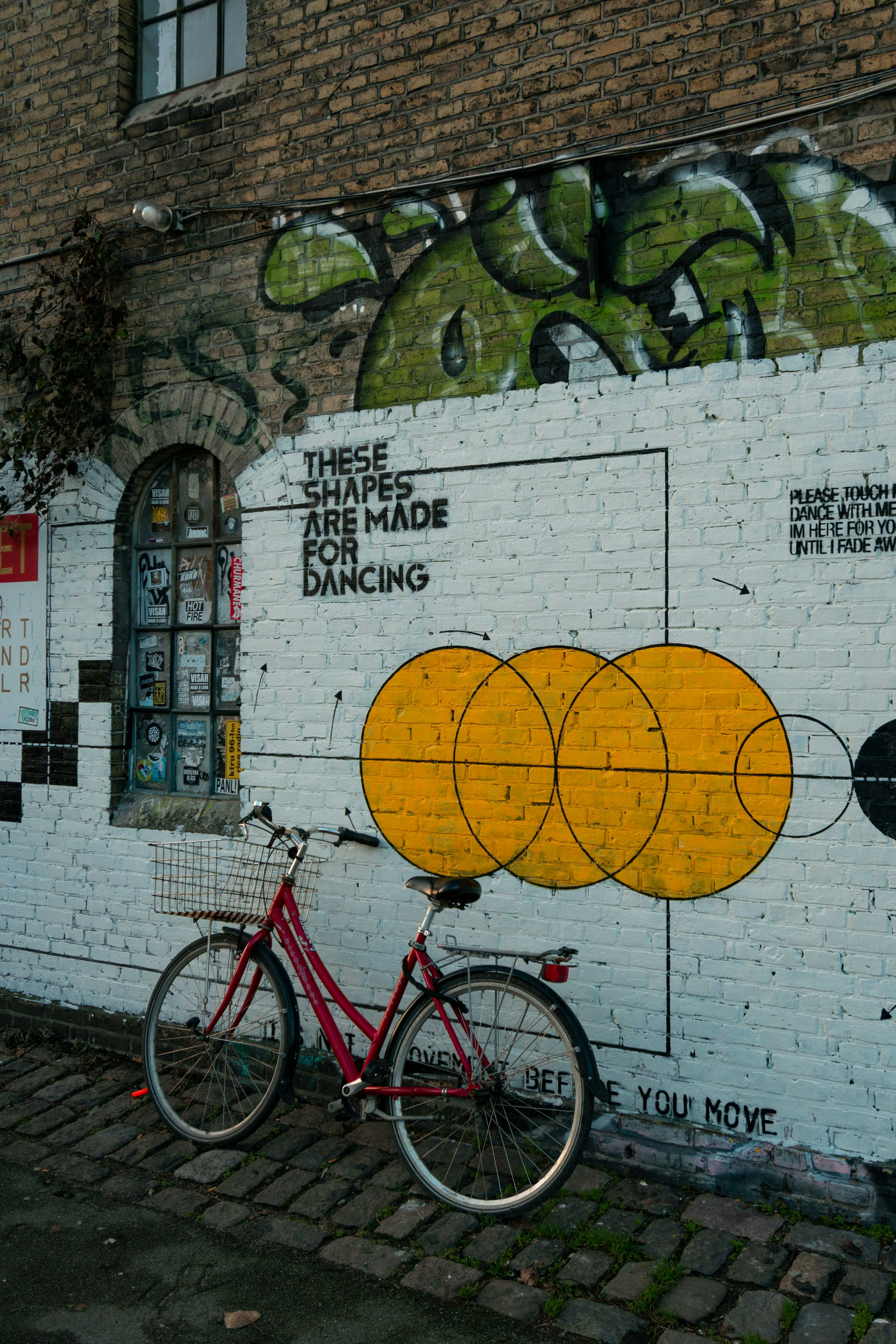 A red bicycle with a basket parked against a white brick wall with graffiti