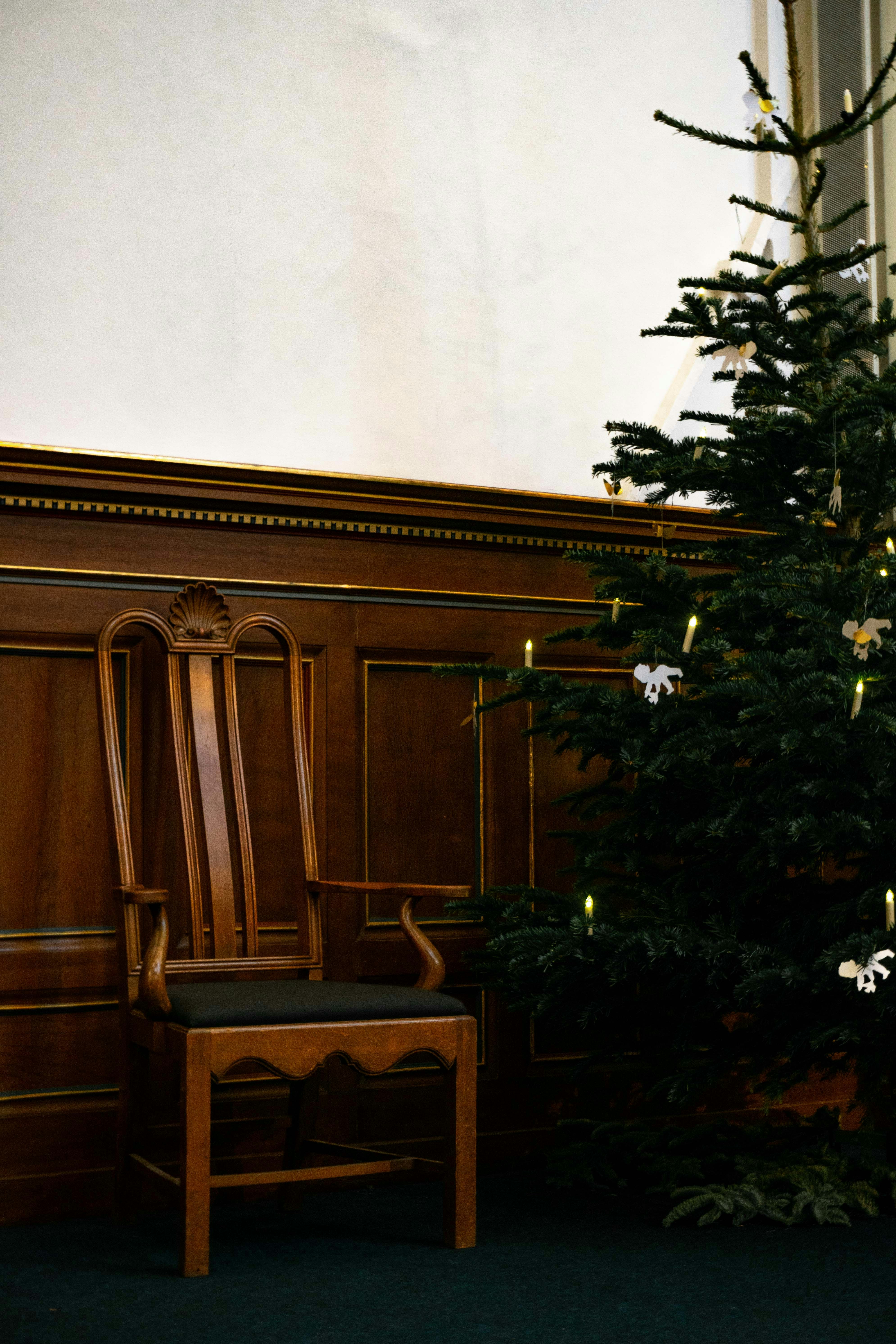 A wooden chair beside a Christmas tree with small lights and white ornaments