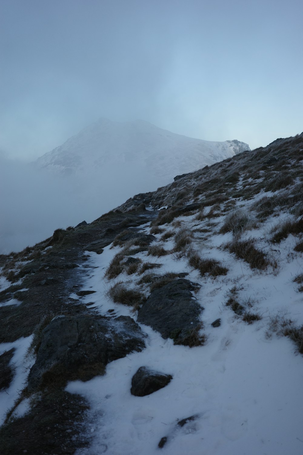 a snow covered mountain side with rocks and grass