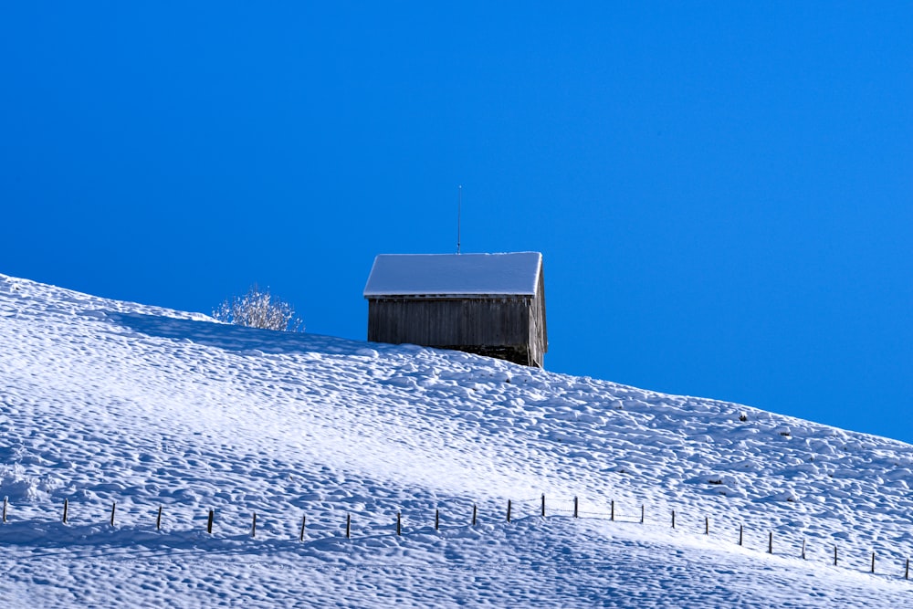 a barn on a snowy hill with a blue sky in the background