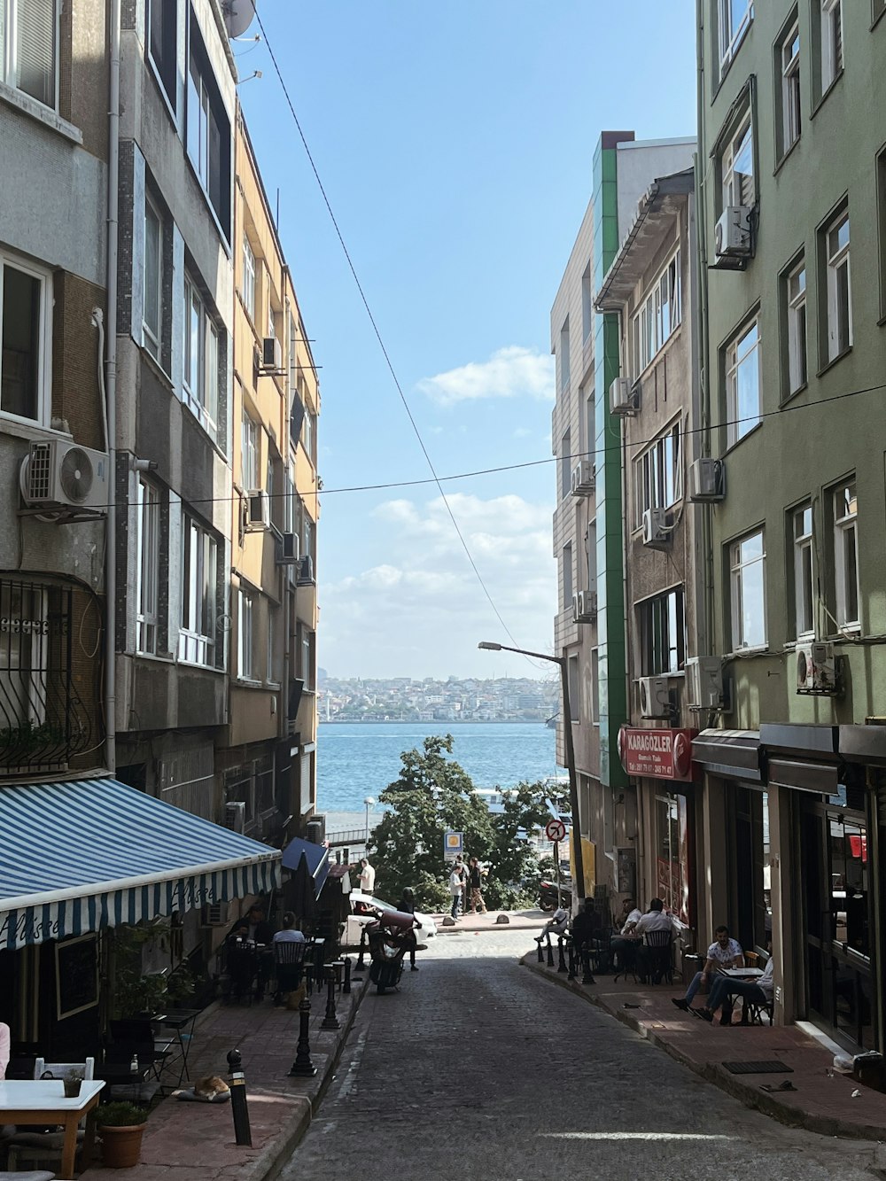 a narrow city street with people sitting on benches