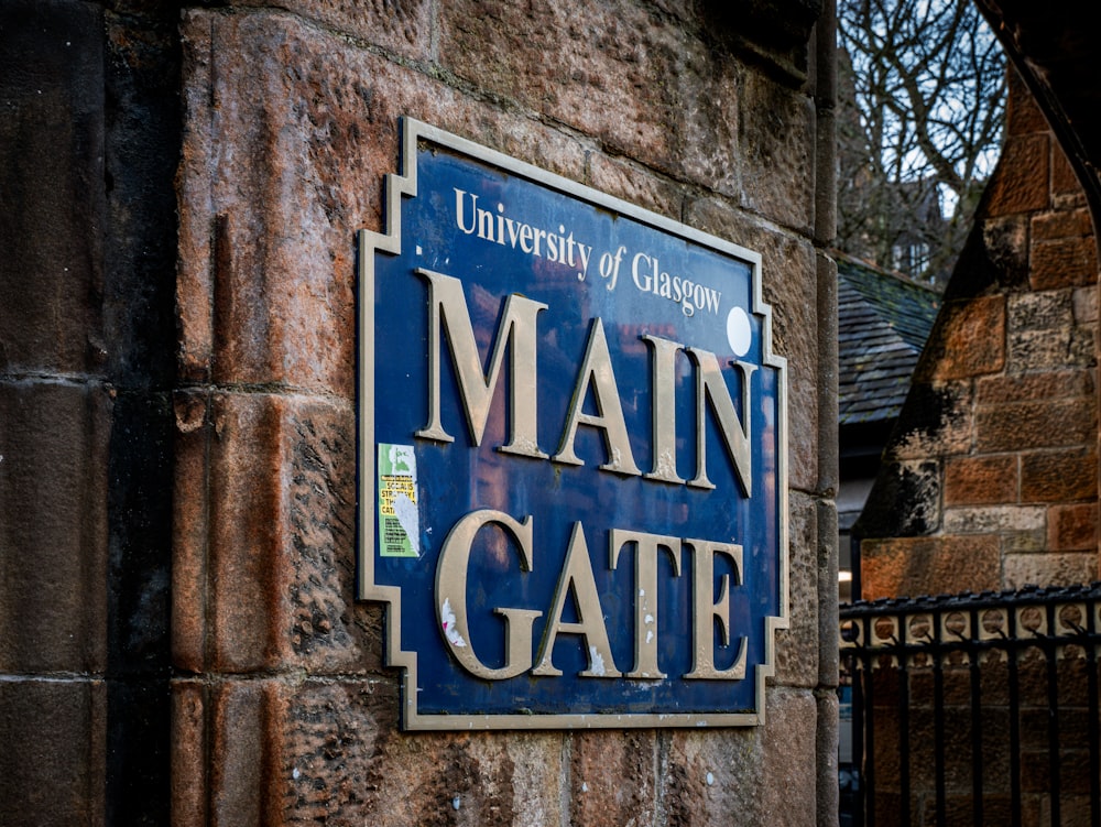 a blue sign that reads main gate on a brick wall