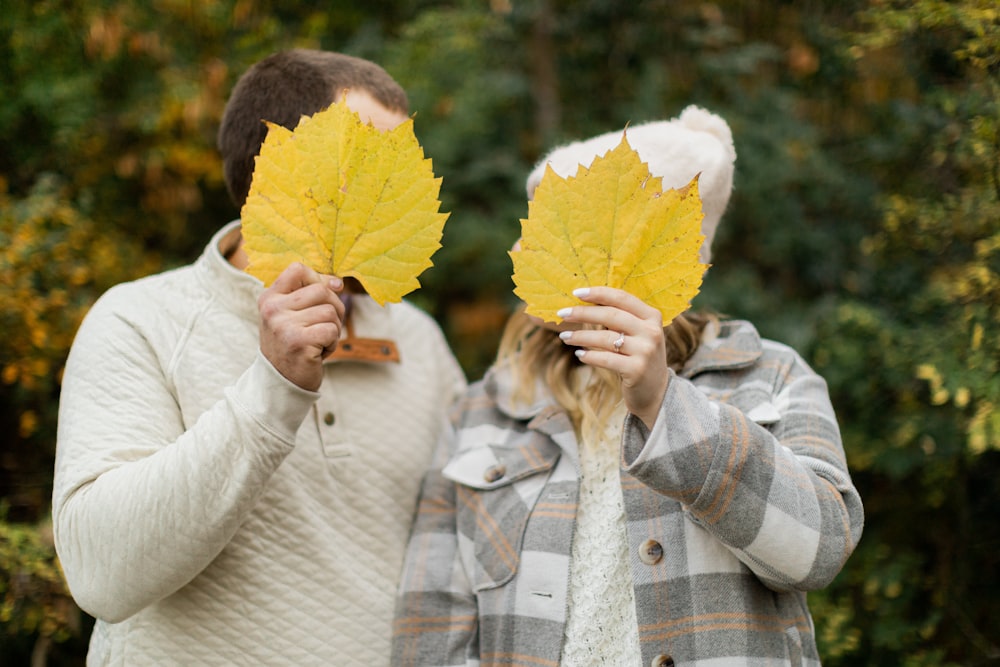 two people holding up yellow leaves in front of their faces