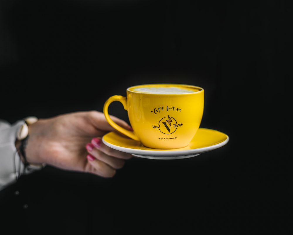 a person holding a yellow coffee cup and saucer