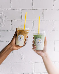 two people holding up drinks in front of a brick wall