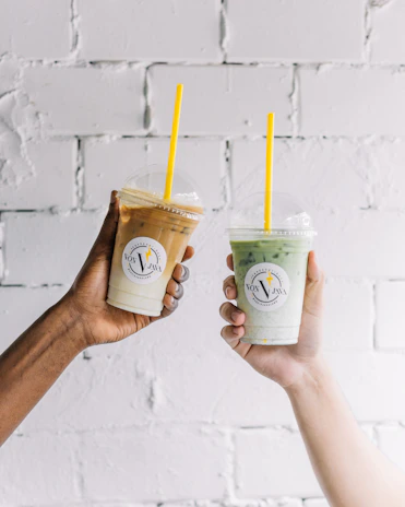 two people holding up drinks in front of a brick wall