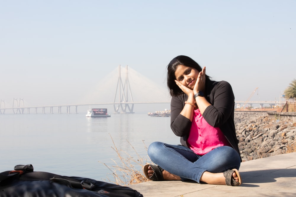 a woman sitting on the ground next to a body of water