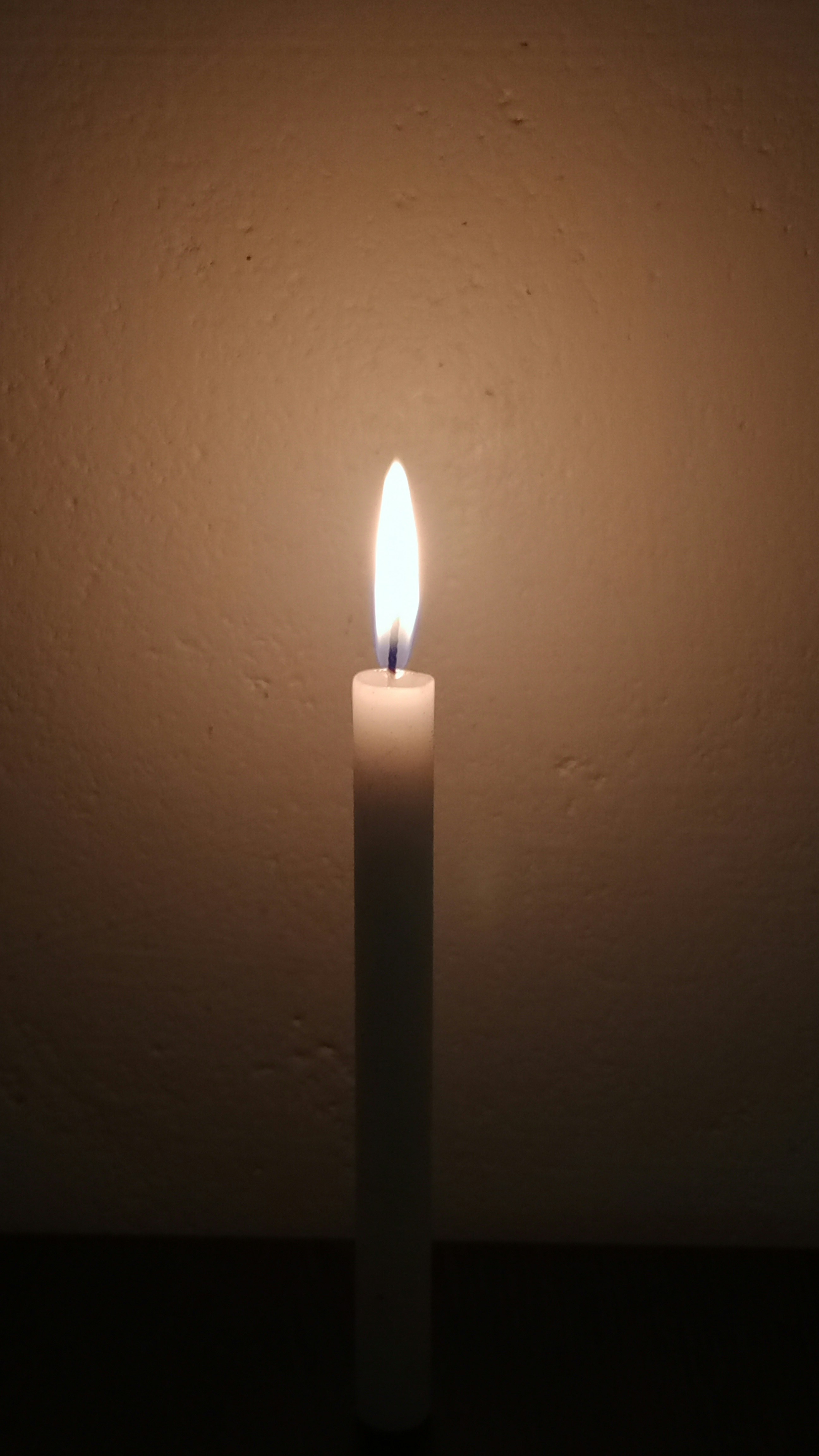Single candle flame in dark church interior, solitary and contemplative, warm glow against stone walls