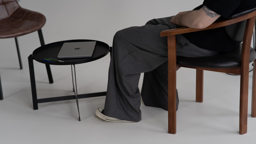 a man sitting in a chair next to a table with a laptop on it