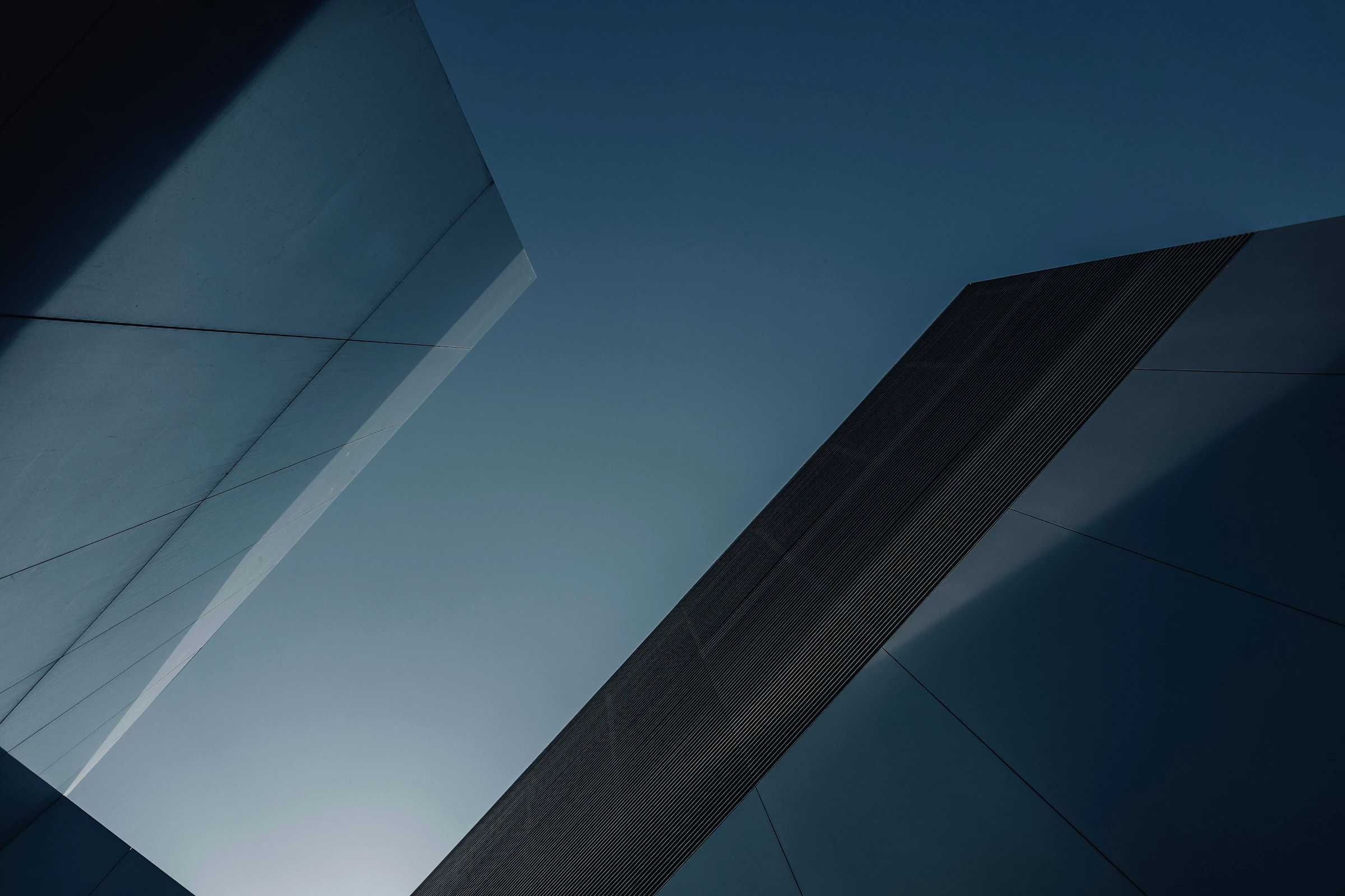 The angular aluminium facade of a modern building cutting into a deep blue dusk sky